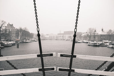 Sailboats moored on river by buildings in city against sky