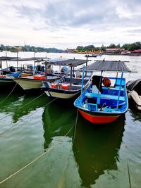 Fishing boats moored at harbor against sky