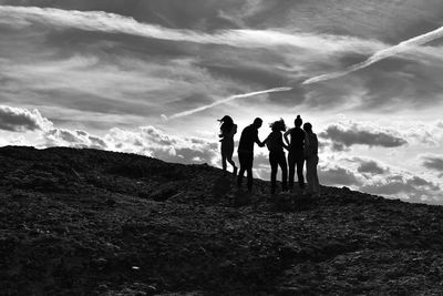 Silhouette friends on hill against cloudy sky