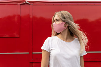 Close-up of woman wearing flu mask looking way standing against red background