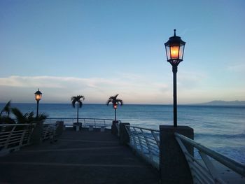 Street light by sea against sky at dusk