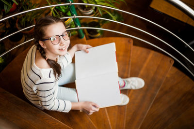 Girl in glasses with a book in her hands sitting on the stairs