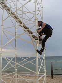 Mid adult man climbing on metallic structure of lookout tower at beach