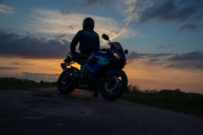 Low angle view of man by motorcycle against sky during sunset