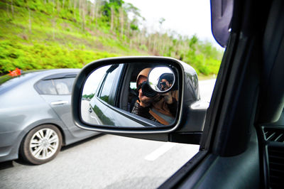 Reflection of woman photographing in side-view mirror