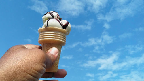 Low angle view of hand holding ice cream against blue sky