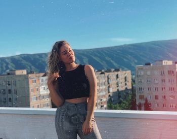 Beautiful young woman standing on city against sky