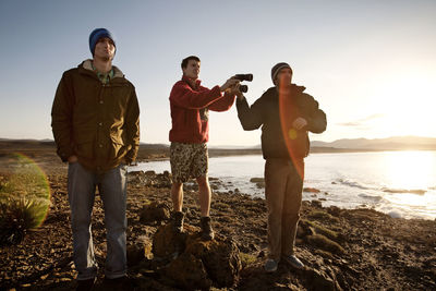 Friends standing on rocky sea shore against sky