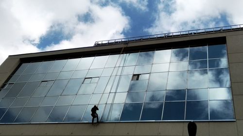 Low angle view of people walking on modern building against sky