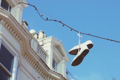 Low angle view of shoes hanging on cable against clear sky