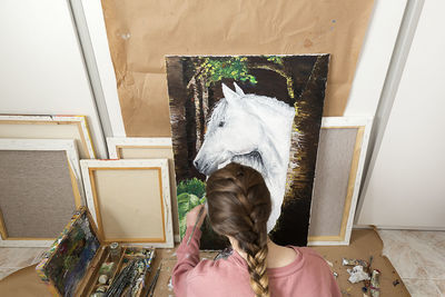 High angle view of teenage girl painting horse on canvas at home