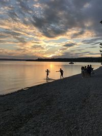 Silhouette people on beach against sky during sunset