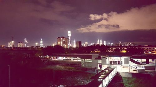 Illuminated bridge over river by buildings against sky at dusk