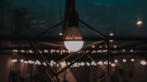 Close-up of illuminated light bulb hanging from ceiling