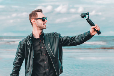 Man wearing sunglasses standing against sea