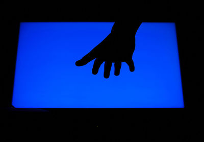 Cropped image of silhouette hand against clear sky in darkroom