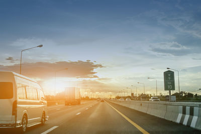 Vehicles on highway against cloudy sky during sunset