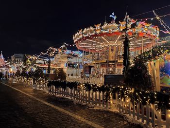 Illuminated ferris wheel by city against sky at night