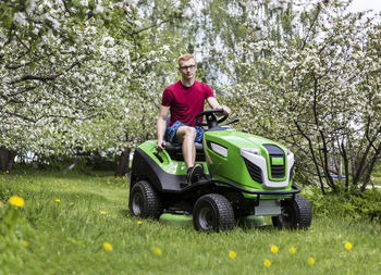 Young man riding lawn mower at grassy field