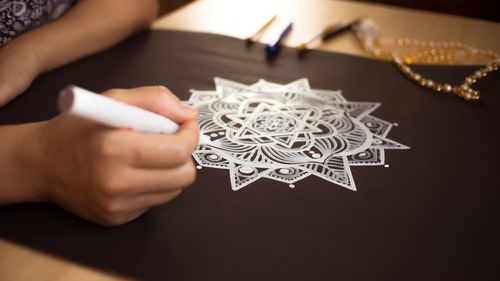 Cropped hands of woman drawing on black paper at table