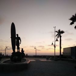 Silhouette statues in city against sky during sunset