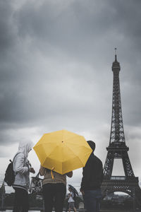 Low angle view of people by eiffel tower against cloudy sky