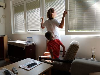 Mother and son looking through window at home