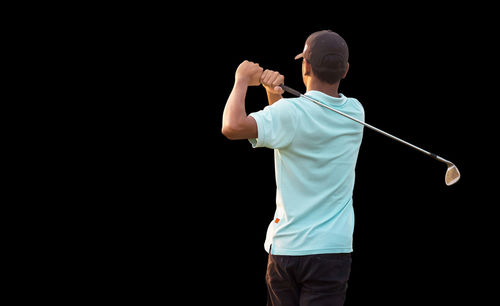 Rear view of man playing golf against black background