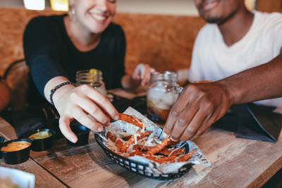 Group of diverse friends gathering at table and eating delicious potato with cheese and bacon from plate