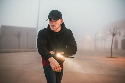 Man with cap on electric scooter during a foggy day