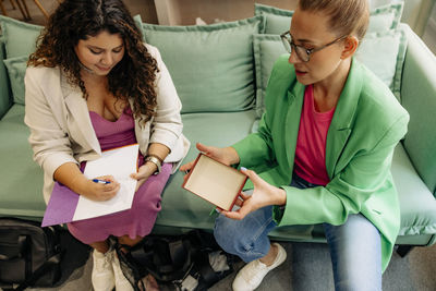 High angle view of female boss discussing with colleague over box while sitting on sofa at office