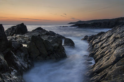 Scenic view of rocks in sea against sky during sunset