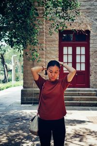 Woman tying hair while standing against building