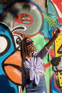 Beautiful woman holding leaf while standing against graffiti wall