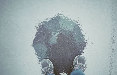 Low section reflection of man standing with umbrella in rain