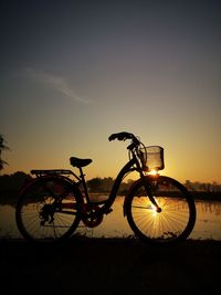 Silhouette bicycle on street against sky during sunset