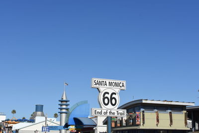 Low angle view of sign by building against clear blue sky