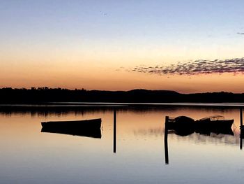 Silhouette wooden posts in lake against sky during sunset