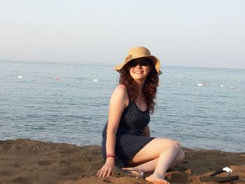 Woman sitting by sea against clear sky