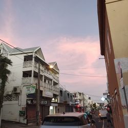 Cars on road by buildings against sky during sunset