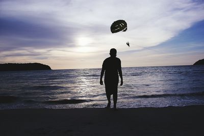Silhouette man at beach with people parasailing over sea against sky