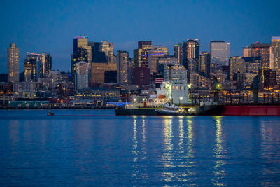 Illuminated buildings by sea against blue sky