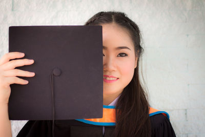 Portrait of a smiling young woman holding camera against wall