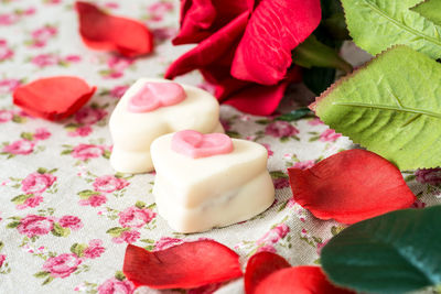 Close-up of heart shape chocolates by red rose petals on table
