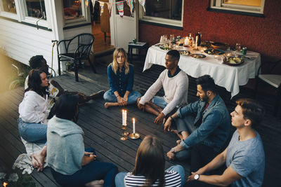 High angle view of male and female friends sitting with eyes closed around lit candles in balcony during group therapy s