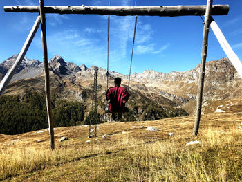 Rear view of man swinging over mountain against sky