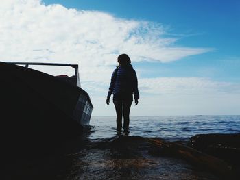 Rear view of man standing on sea shore against sky