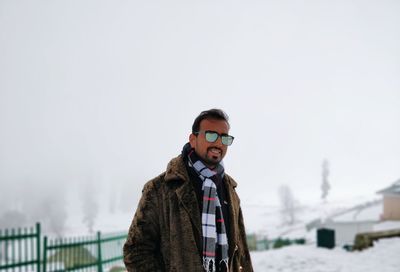 Portrait of young man in warm clothing wearing sunglasses while standing on snow against sky