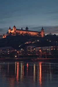 Illuminated buildings by river against sky at night