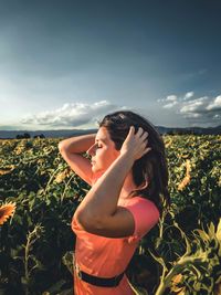 Side view of young woman looking away while standing against sky